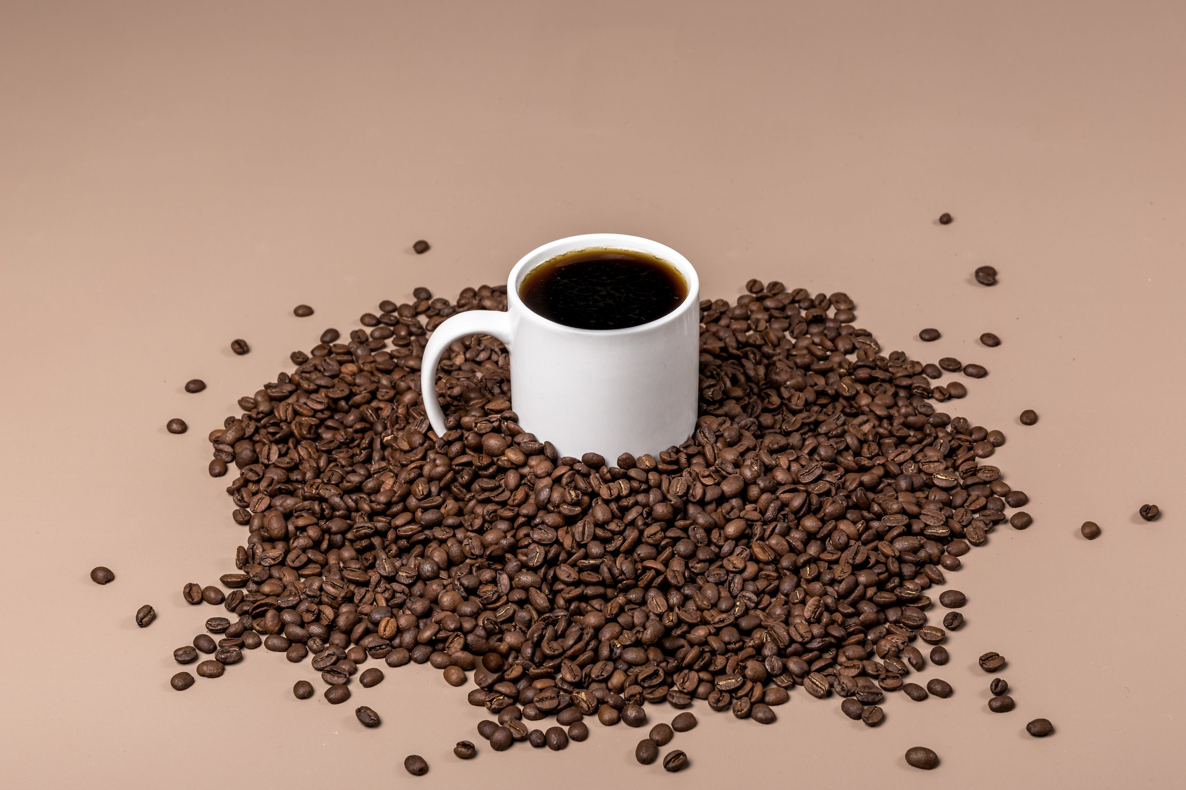 Cup full of coffee sitting in a bed of roasted coffee beans